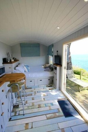 A compact room with a bed, a small desk, a chair, and a view of the sea.