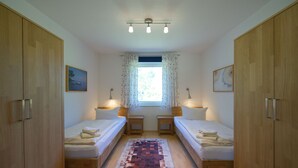 Una habitación con dos camas, una ventana con cortinas, una lámpara en el techo y un cuadro en la pared.