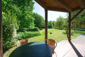Un espace extérieur aménagé en patio, doté d’un coin salon couvert, et entouré d’une végétation luxuriante et d’arbres.