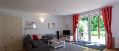 Ein modernes Wohnzimmer mit einer Couch, einem Couchtisch und einem Fernseher, einer Schiebetür zu einem Garten und einem weißen Schrank.