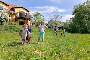 Une famille joue dans une cour verdoyante, avec une maison en arrière-plan.