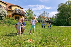 A family playing in a grassy yard with a house in the background. - 2-room vacation apartment, 2 (+2) persons, ground floor (13) - Müritzparadies - Feriendorf (Rechlin)