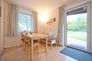 A dining area with a wooden table and chairs, a lamp, and a view of a garden through a sliding glass door.
