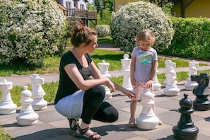 Une femme et un enfant jouent avec des pièces d’échecs surdimensionnées dans un jardin.