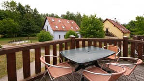 A wooden deck with a table and four chairs, overlooking a garden with chess pieces and two houses.