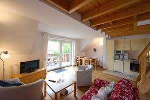 Un salon confortable avec une télévision, un canapé et une table basse. Il y a également un coin repas avec des chaises et une table, ainsi qu'une cuisine équipée de placards et d'appareils électroménagers.