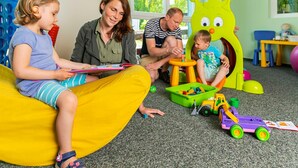 A family in a playroom with a child on a bean bag, another child playing with toys, and an adult supervising. - 2-room vacation apartment, 6 persons, balcony, upper floor (4) - Müritzparadies - Feriendorf (Rechlin)
