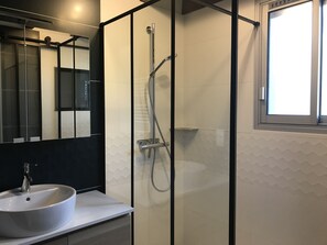 A modern bathroom with a glass-enclosed shower, a white sink, and a large mirror.