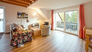 Un salon spacieux avec un plafond en bois, une grande fenêtre avec des rideaux, un canapé, un fauteuil et une table basse.