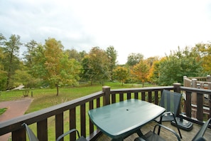 Une terrasse avec une table et des chaises, donnant sur un espace verdoyant agrémenté d’arbres et d’un sentier.