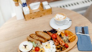 A wooden table with a breakfast plate, a cup of coffee, and a napkin. - Hotel Golden Square Bishkek (Bishkek)