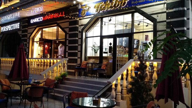 An outdoor seating area with tables and chairs, a staircase leading to an upper level, and a building with a coffee shop sign. - Hotel Golden Square Bishkek (Bishkek)