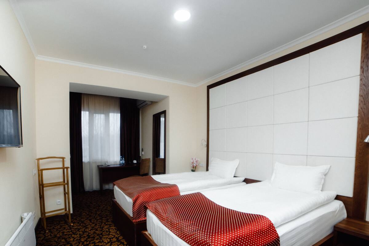 A hotel room with two beds, a TV mounted on the wall, a desk, and a chair.