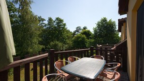 An outdoor patio with a table and chairs, surrounded by a wooden fence, overlooking a garden with trees. - 2-room vacation apartment, 6 persons, balcony, upper floor (12) - Müritzparadies - Feriendorf (Rechlin)