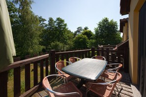 Eine Terrasse im Freien mit Tisch und Stühlen, umgeben von einem Holzzaun, mit Blick auf einen Garten mit Bäumen.