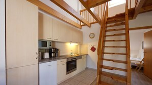 A kitchen with a microwave, toaster, and oven. There is a wooden staircase leading to a loft bedroom. - 2-room vacation apartment, 6 persons, balcony, upper floor (12) - Müritzparadies - Feriendorf (Rechlin)