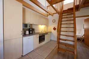 Eine Küche mit Mikrowelle, Toaster und Backofen. Eine Holztreppe führt zu einem Schlafzimmer im oberen Bereich.