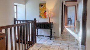 A hallway with a wooden railing, a black console table with a lamp, and a painting on the wall.