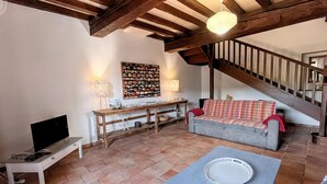 A cozy living room with a wooden ceiling, a grey sofa, a small table, and a staircase.