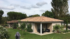 A small house with a tiled roof, a covered patio with outdoor furniture, and a well-maintained lawn.