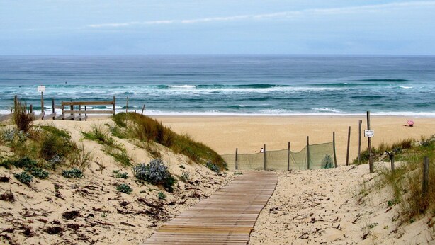 A wooden boardwalk leading to a sandy beach with ocean waves in the background.