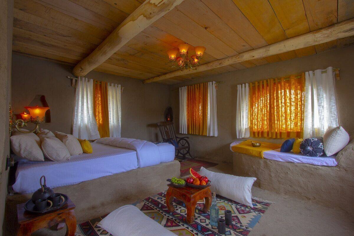 A cozy room with two beds, a small table with a teapot, and a window with curtains.