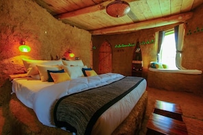 Un dormitorio acogedor con cama, cabecera de madera, ventana con cortinas y una lámpara de pared.