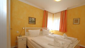 A hotel room with a single bed, a bedside table, a nightstand, and a window with curtains. - Haus Sonnenschein, Germany (Sylt)