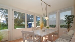 A sunlit patio with a white table and chairs, a sofa, and a hanging light fixture. - Haus Sonnenschein, Germany (Sylt)