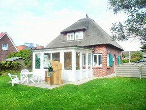 A house with a thatched roof, a covered patio with white furniture, and a brick exterior. - Haus Sonnenschein, Germany (Sylt)