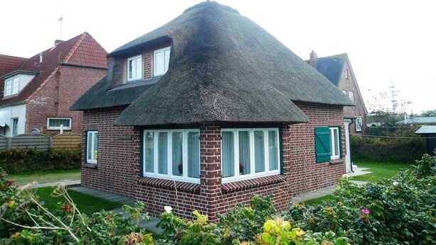 A house with a steeply pitched roof, brick exterior, and a small garden area with flowers. - Haus Sonnenschein, Germany (Sylt)