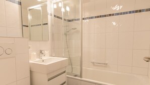 A modern bathroom with a glass-enclosed shower, a white sink, and a bathtub. - Südstrand 3, Germany (Sylt)