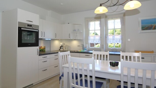 A modern kitchen with white cabinetry, a black oven, and a dining table with white chairs. - Südstrand 3, Germany (Sylt)