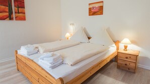 A wooden bed with white linens and towels, two bedside tables with lamps, and two paintings on the wall. - Südstrand 3, Germany (Sylt)