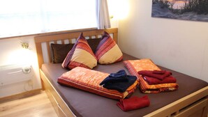 Un lit avec un cadre en bois, deux oreillers, une couverture et une serviette pliée.