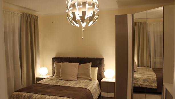 Un dormitorio con una cama grande, dos lámparas de noche, un espejo y una lámpara esférica original.