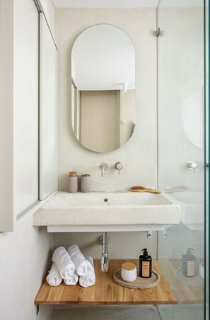 A bathroom with a white sink, a mirror, and a wooden shelf with towels and toiletries.