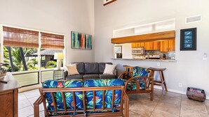 A spacious living area with a sofa and chairs, a kitchen with wooden cabinets, and a balcony with a view of greenery. - Kanaloa at Kona 1606: Beautiful Oceanview Condo w/ Shared Pool, Spa, AC & Lanai (Kailua Kona)