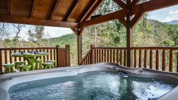 Un jacuzzi bajo un porche de madera con vistas a una ladera boscosa.