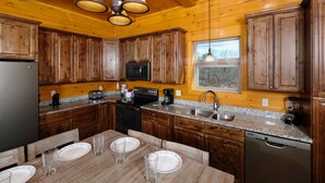 Cocina de cabaña de madera con encimeras de granito, gabinetes de madera, un refrigerador negro, una estufa, un fregadero y un lavavajillas.