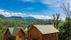 Una cabaña rústica con techo verde ubicada en un valle boscoso, rodeada de montañas.