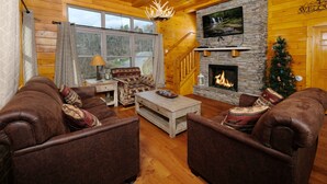 Un acogedor interior de cabaña de troncos con chimenea, sofás de cuero, televisor y un árbol de Navidad.