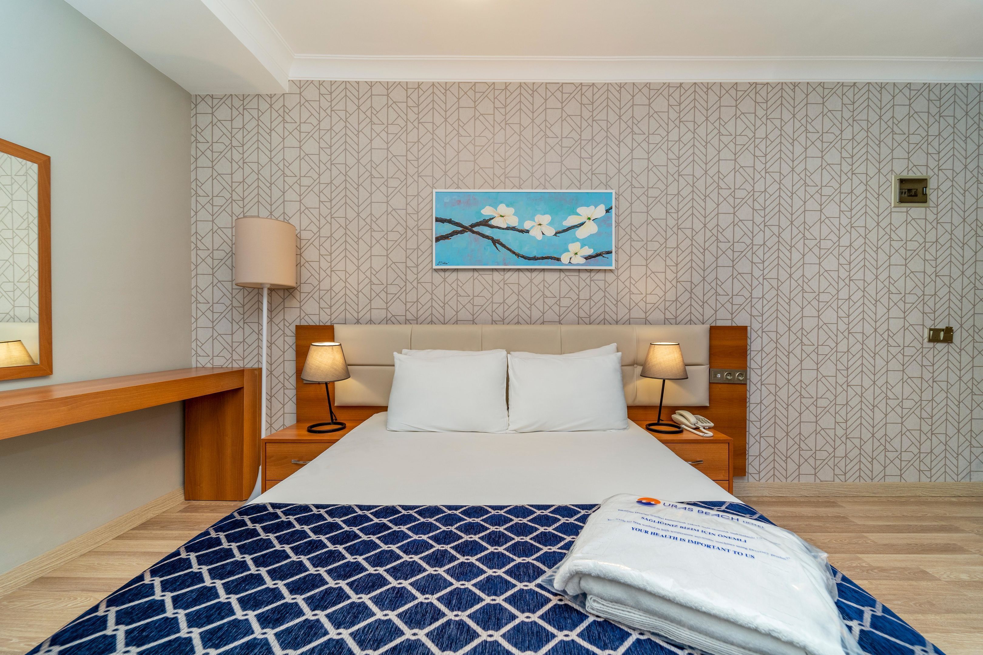 A hotel room with a bed, two bedside tables with lamps, a wall-mounted painting, and a wooden nightstand.