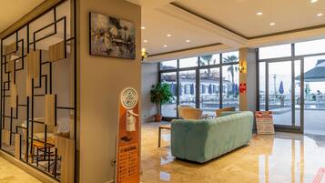 A hotel lobby with a reception desk, seating area, and large windows offering a view of the street.