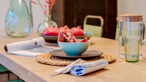 Uma mesa de madeira com uma tigela de frutas, um jarro de vidro e um quadro pendurado na parede.