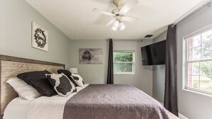 A bedroom with a bed, a ceiling fan, a TV, and a window with curtains. - The Flo's house, Snowbird Winter Haven • Spacious 1800 sq ft Home with New Lanai (Tampa)