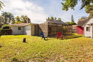 A backyard with a covered patio, a red chair, and a small shed.
