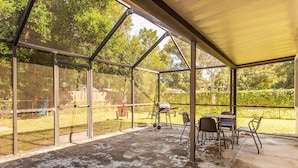 A covered patio with a table and chairs, a grill, and a view of a backyard with a fence and trees. - The Flo's house, Snowbird Winter Haven • Spacious 1800 sq ft Home with New Lanai (Tampa)