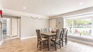 A dining area with a wooden table and chairs, a window with a view of the outdoors, and a door leading to another room. - The Flo's house, Snowbird Winter Haven • Spacious 1800 sq ft Home with New Lanai (Tampa)
