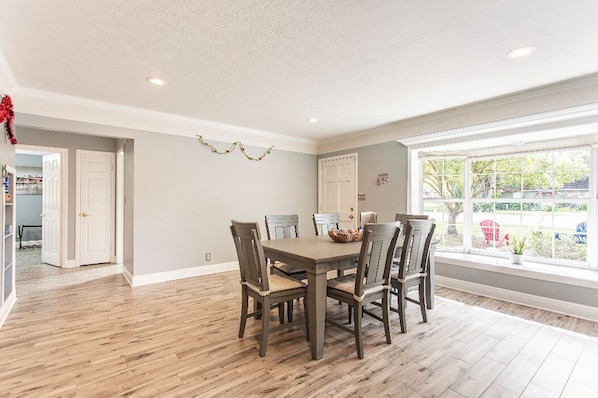 A dining area with a wooden table and chairs, a window with a view of the outdoors, and a door leading to another room.